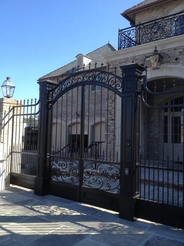 Portón arqueado de hierro con volutas, frente a una casa.