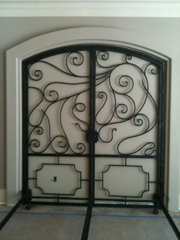 Puerta arqueada de hierro con líneas curvas y ornamentos.