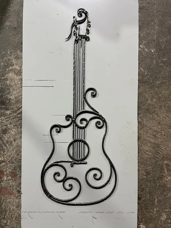 Objeto de metal con forma de guitarra, cuerdas y espirales, colocado sobre una plancha.